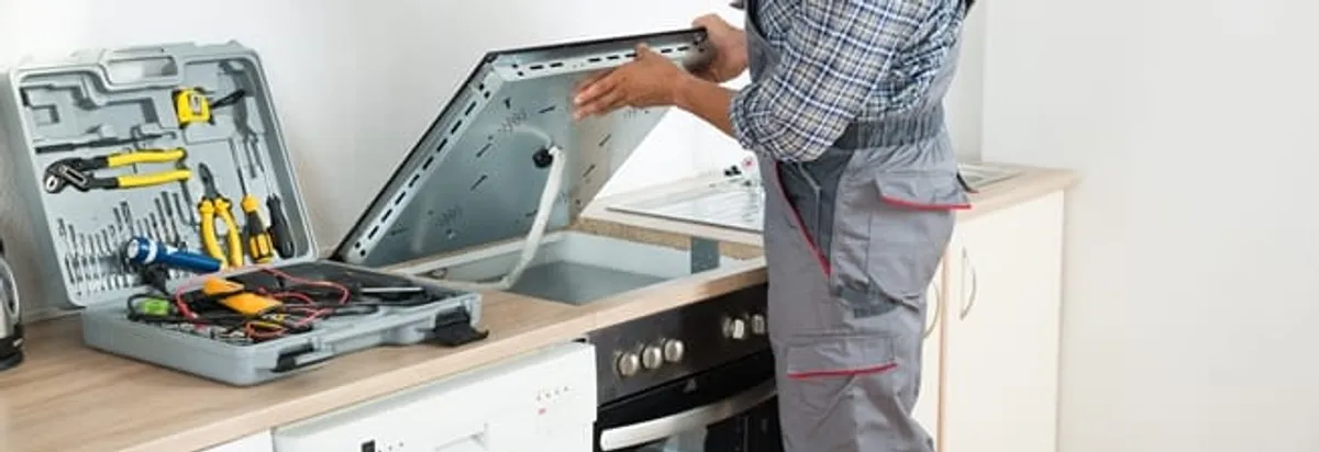 Cooktop repair technician lifting a built-in stovetop for service in Orange, CA