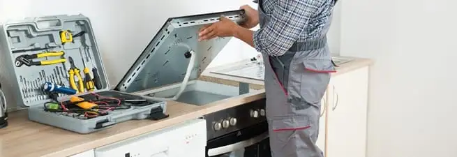 Cooktop repair technician lifting a built-in stovetop for service in Orange, CA