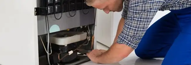 Refrigerator repair technician servicing the compressor and condenser area in Orange, CA