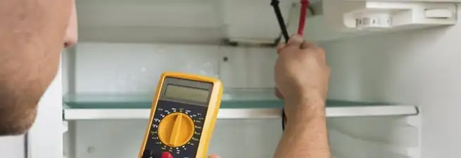 Refrigerator repair technician testing electrical components with a multimeter in Orange, CA