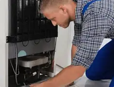 Refrigerator repair technician servicing the compressor and condenser area in Orange, CA